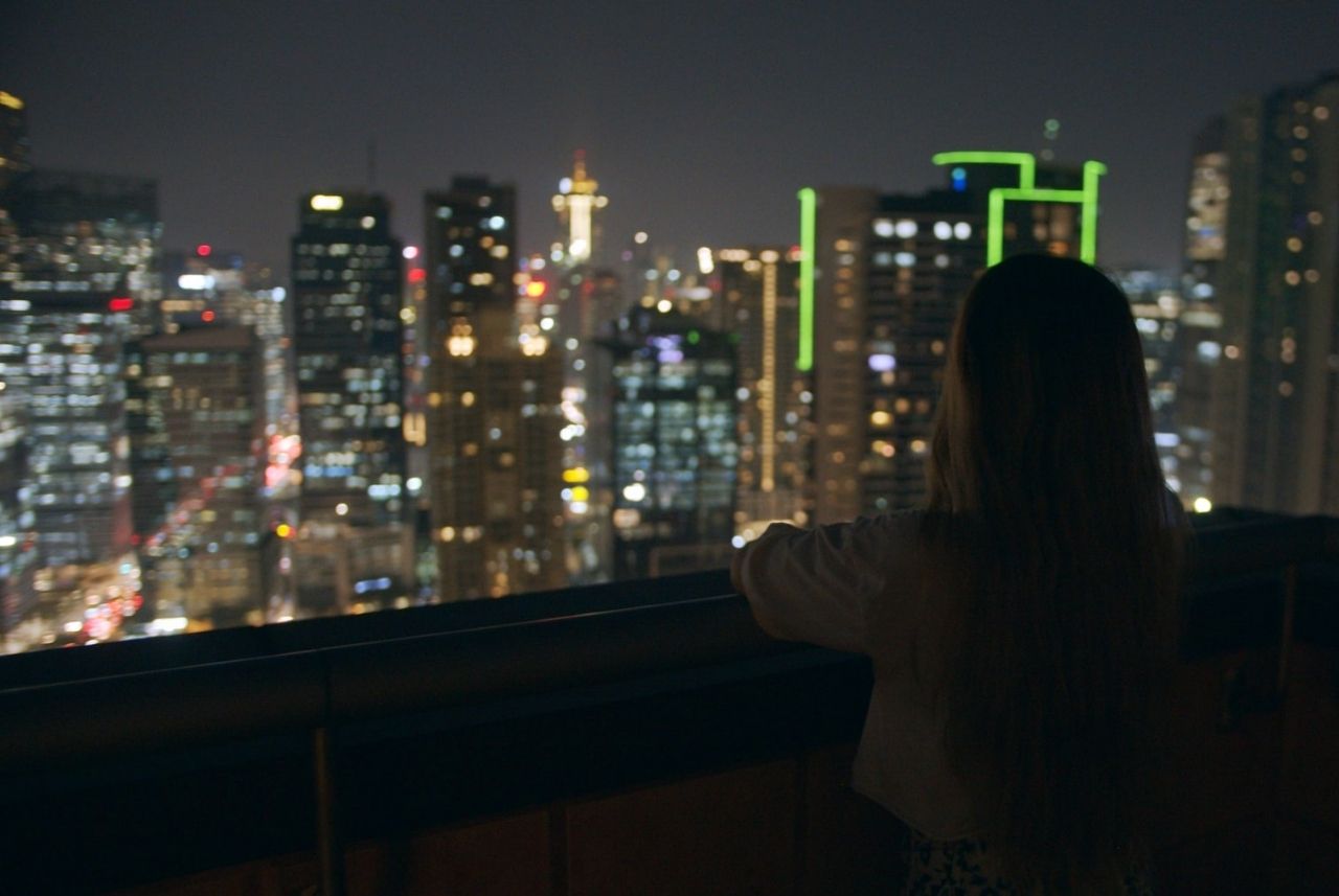Person on a balcony looking over a city skyline at night